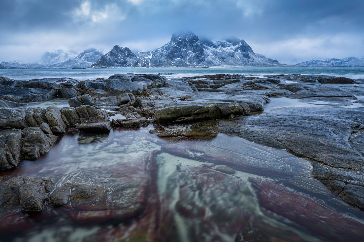 Vareid. Stormy moody sunset in arctic conditions with red stained granite in coastal scene