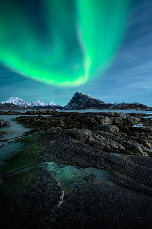 Aurora borealis over a rocky landscape with mountains in the background