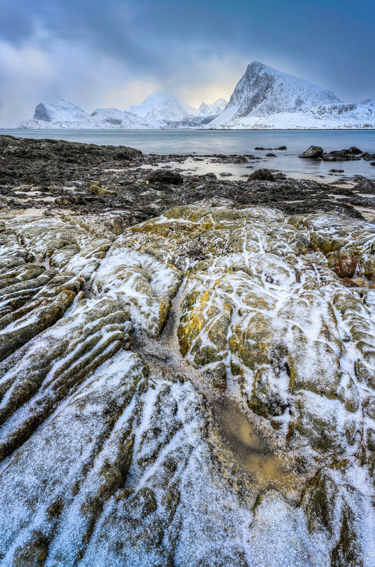 Textured coastal rocks with fresh snow, fjord waters, and dramatic peaks in Lofoten, Norway