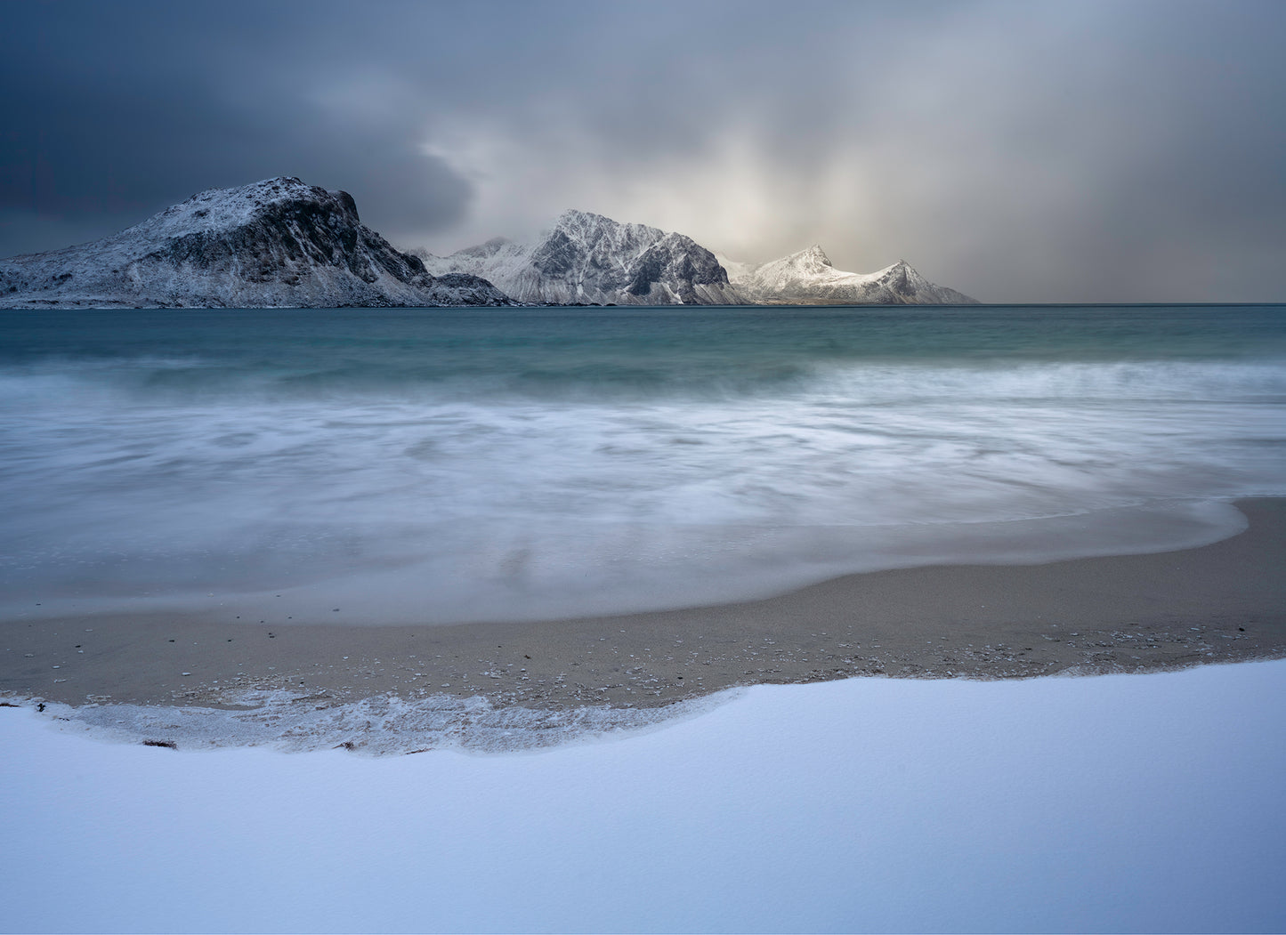 Beach with snow-covered mountains and a cloudy sky