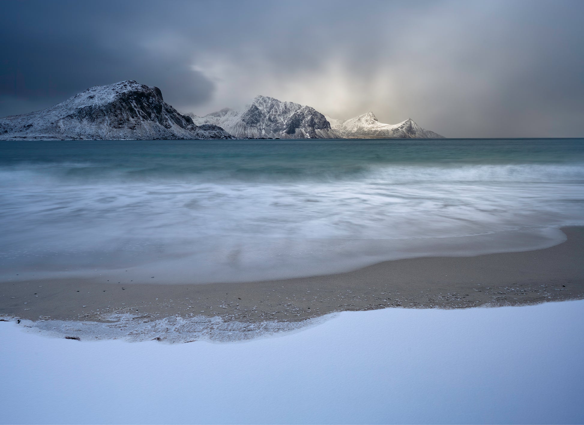 Beach with snow-covered mountains and a cloudy sky