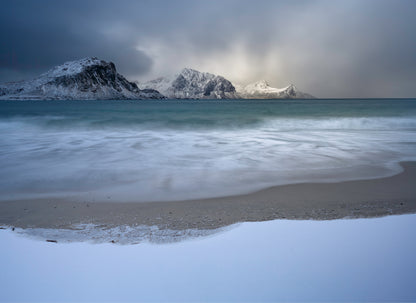 Beach with snow-covered mountains and a cloudy sky