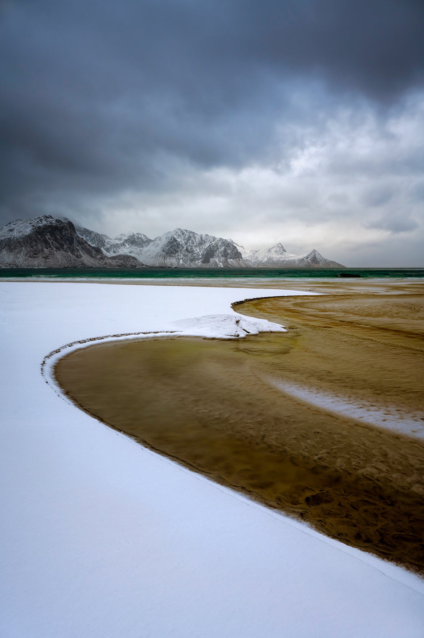 Wetland with snow and mountains under a cloudy sky