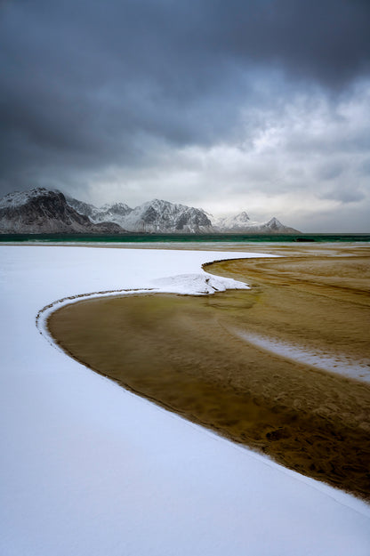 Wetland with snow and mountains under a cloudy sky