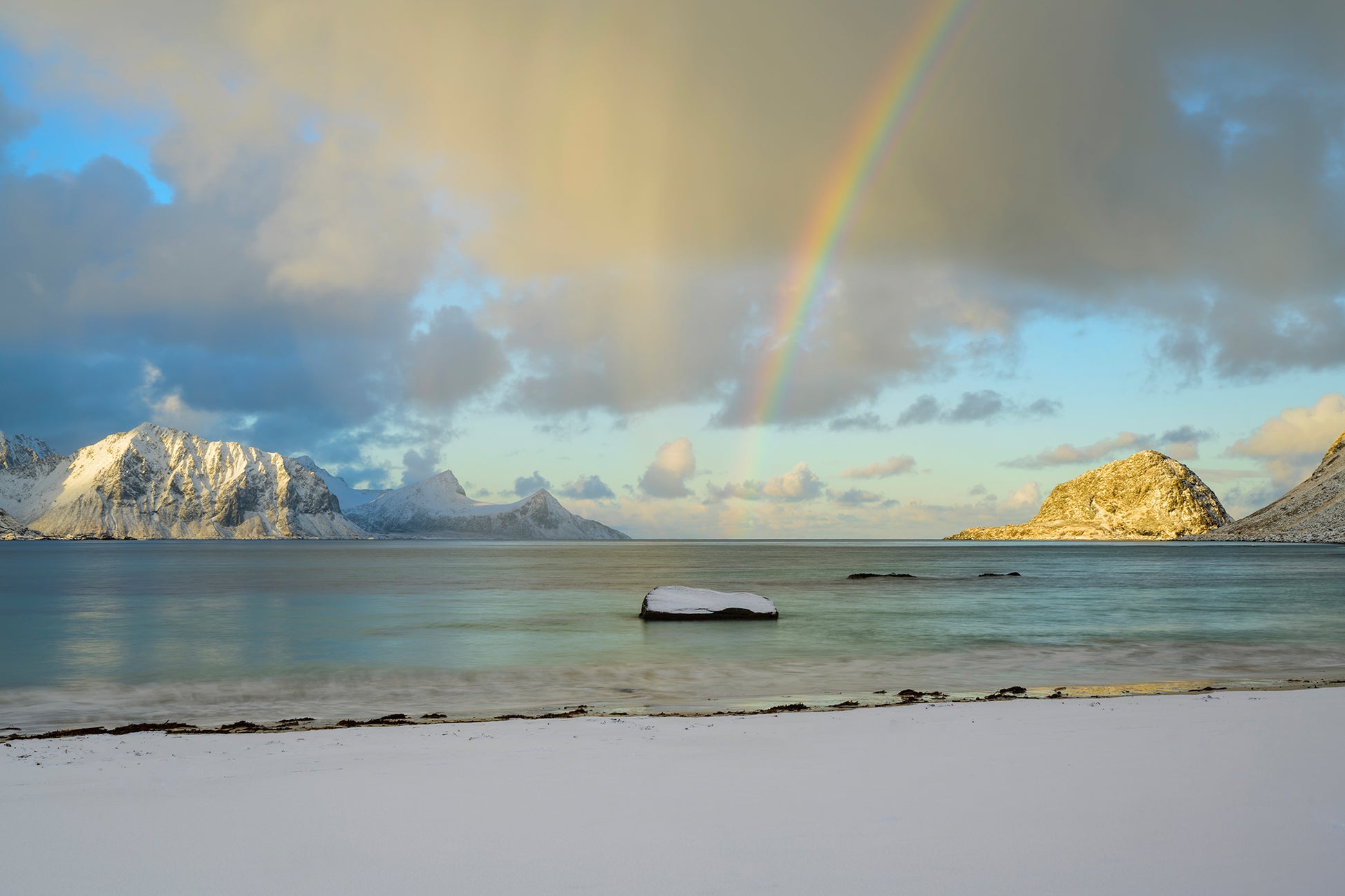 Double rainbow over a snowy landscape with mountains and water.