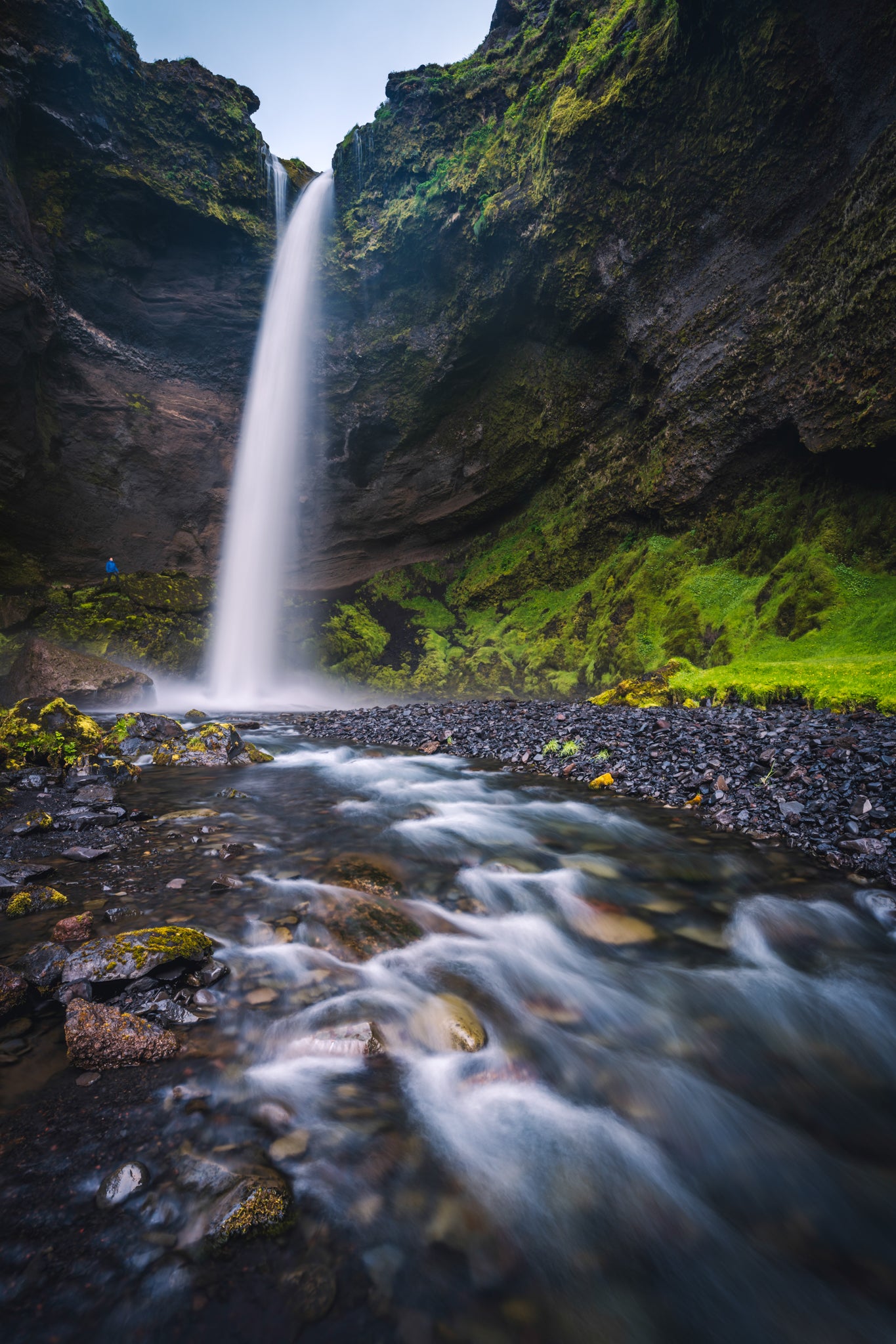 Kvernufoss Waterfall cascading down a rocky cliff into a pool below, surrounded by greenery.