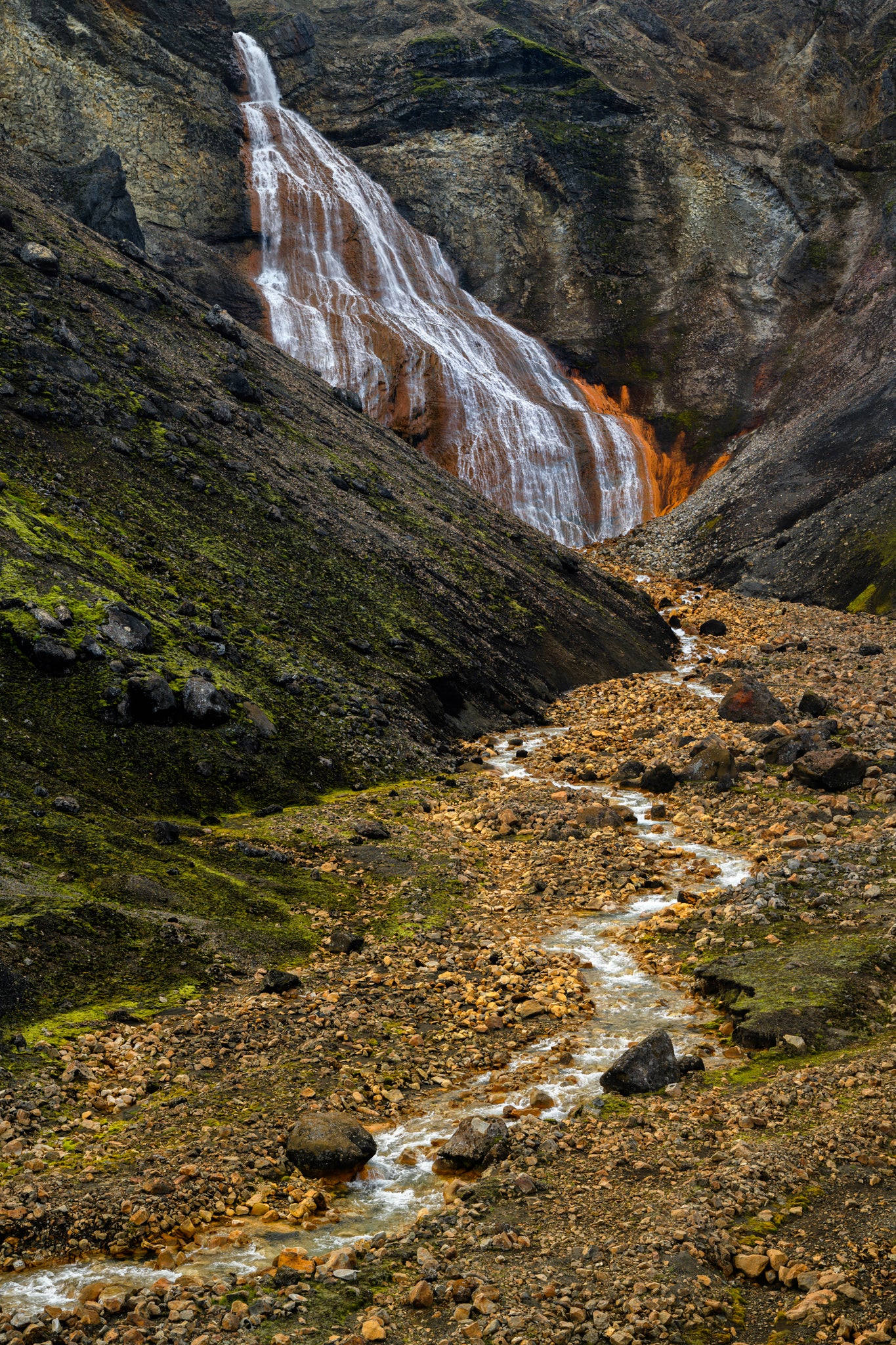 Raudarfoss Waterfall cascading down a rocky mountain with a stream below