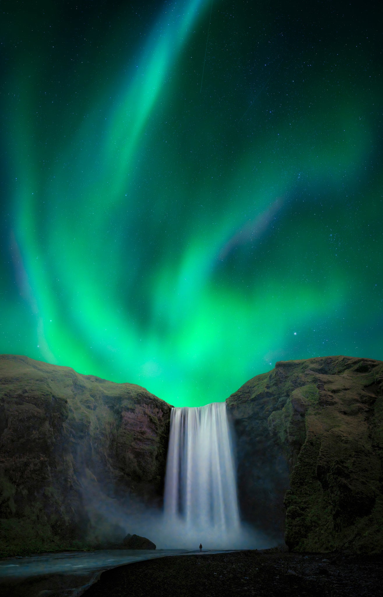Skogafoss. Aurora borealis over a waterfall with rocks in the foreground