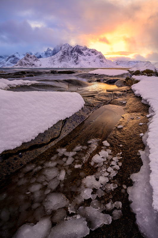 Frozen landscape with snow-covered ground and mountains under a colorful sky.